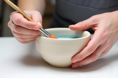 Hände tragen sorgfältig Glasur auf eine Keramikschale auf